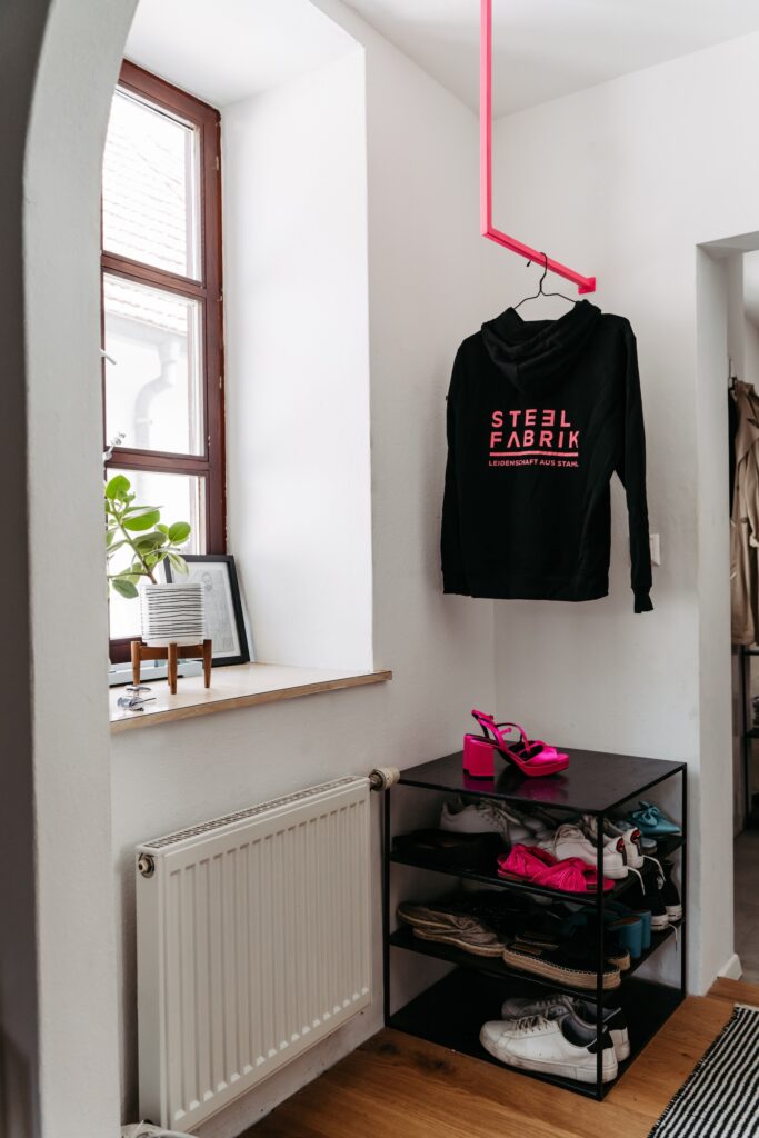 Schwarzer Pulli hängt an einer pinken Kleiderstange über einem Schuhregal