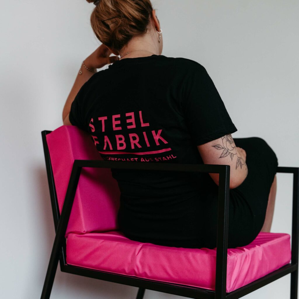 Junge Frau sitzt auf einem schwarzem Loungesessel mit pinker Sitzfläche